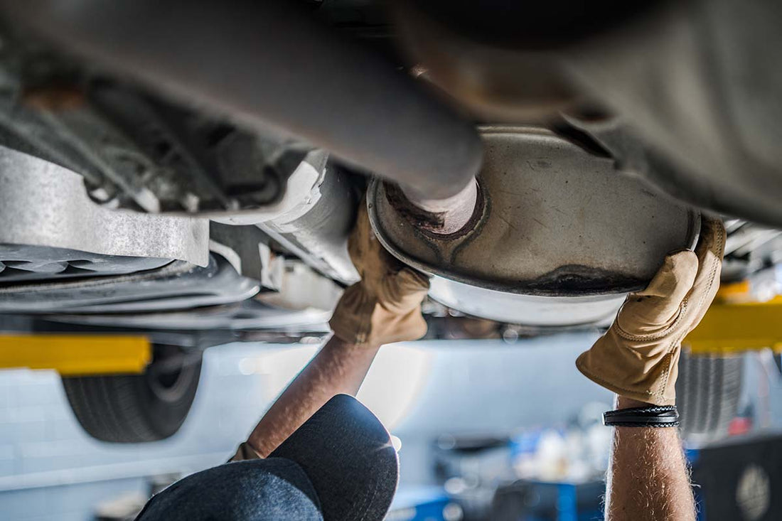 
A mechanic inspecting a vehicle's exhaust system underneaht the car on an lift in a service garage.